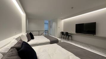 Ein modernes Hotelzimmer mit einem großen Bett, einem kleineren Bett, einem Fernseher und einer Sitzecke mit Sesseln.