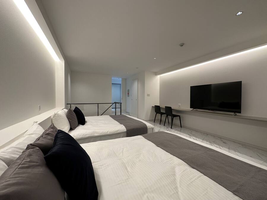 Ein modernes Hotelzimmer mit einem großen Bett, einem kleineren Bett, einem Fernseher und einer Sitzecke mit Sesseln.