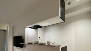 Une cuisine moderne avec un plan de travail blanc, deux tabourets de bar blancs, une hotte noire et un téléviseur à écran plat fixé au mur.