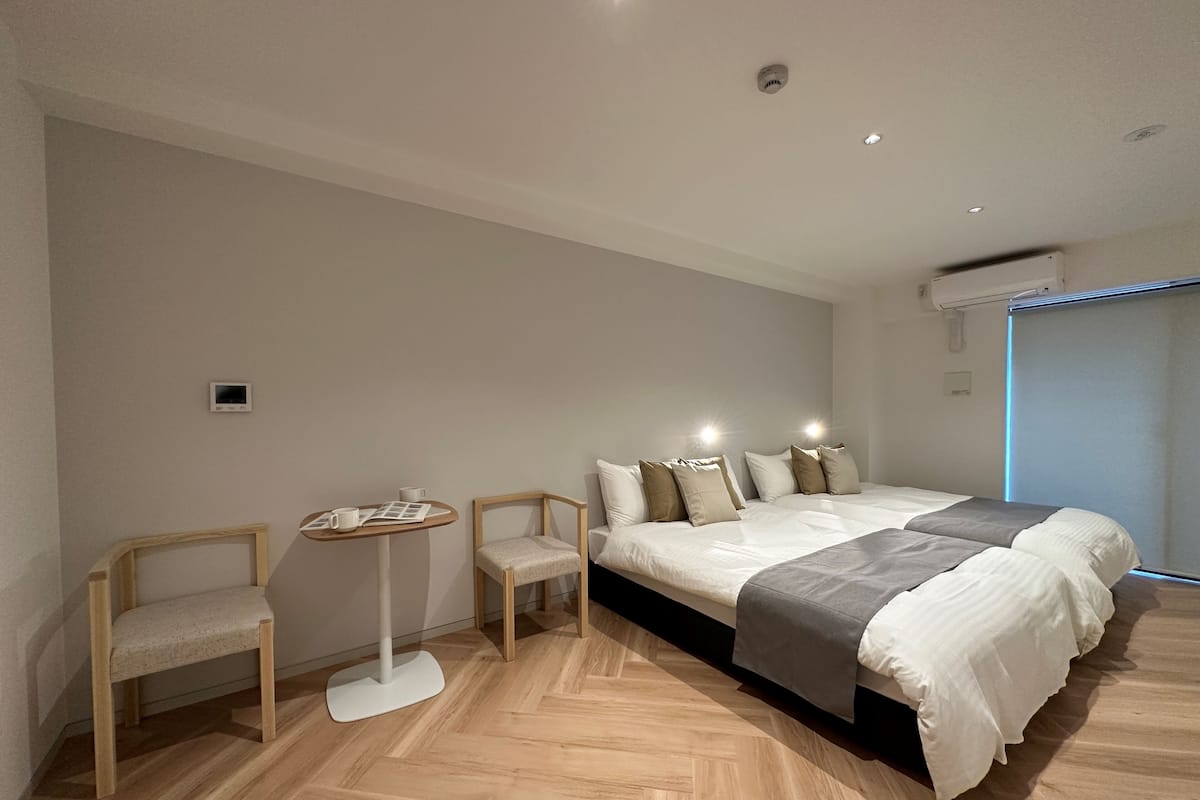 A modern bedroom with a large bed, two chairs, a small table, and a wall-mounted air conditioning unit.