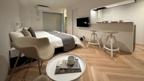 Une chambre d’hôtel moderne équipée d’un lit, d’un bureau, d’une télévision et d’une petite table sur laquelle se trouvent une tasse et un livre.