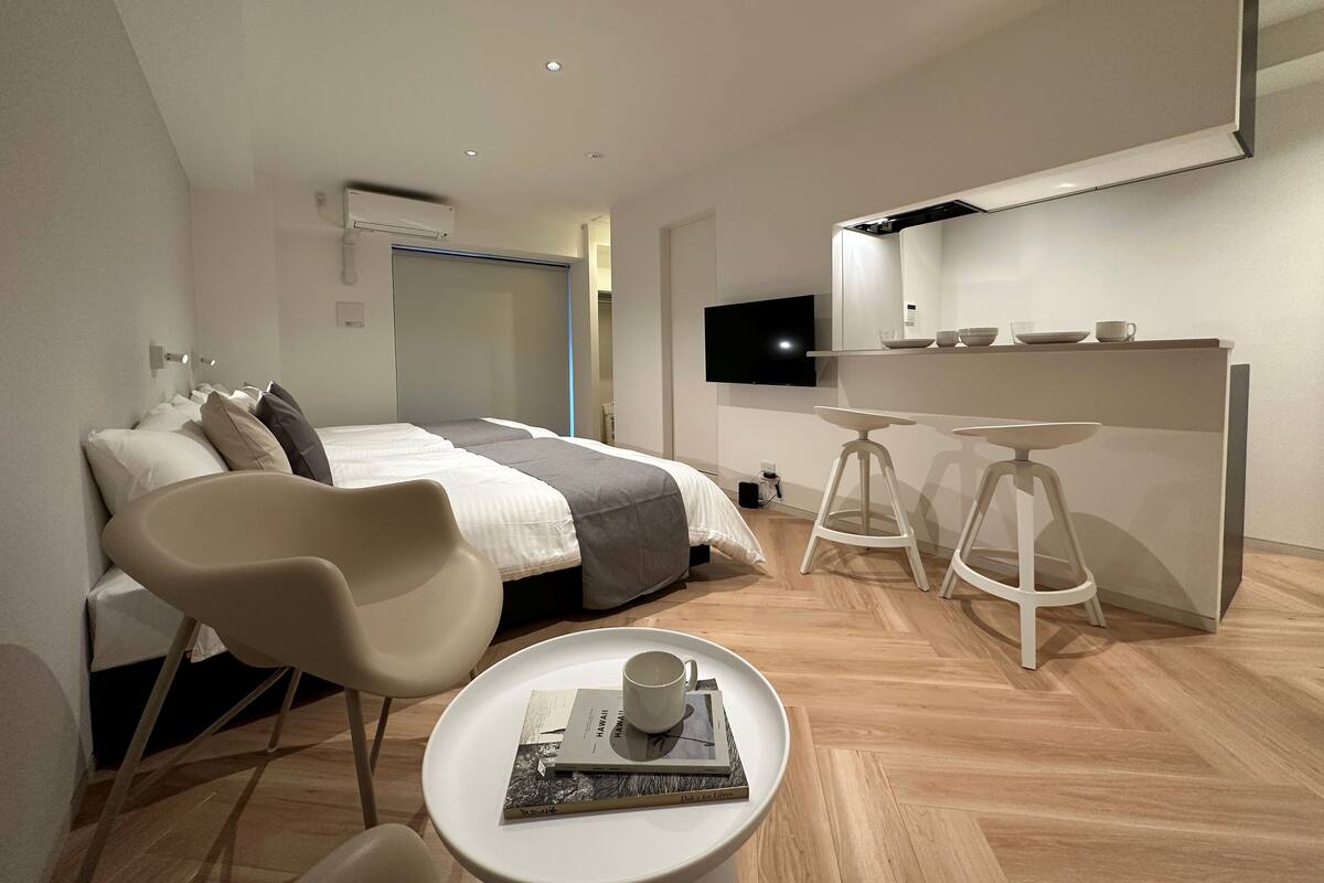 A modern hotel room with a bed, a desk, a TV, and a small table with a cup and book.