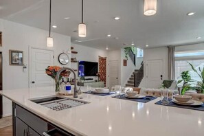 Una cocina moderna con una isla central, electrodomésticos integrados, iluminación colgante y vistas al área de estar.