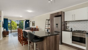 Une cuisine moderne dotée d’un îlot central, d’appareils électroménagers en acier inoxydable et d’un coin repas offrant une vue sur l’extérieur.