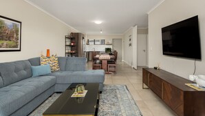 Un salon moderne avec un canapé d’angle, une table basse et un téléviseur fixé au mur.