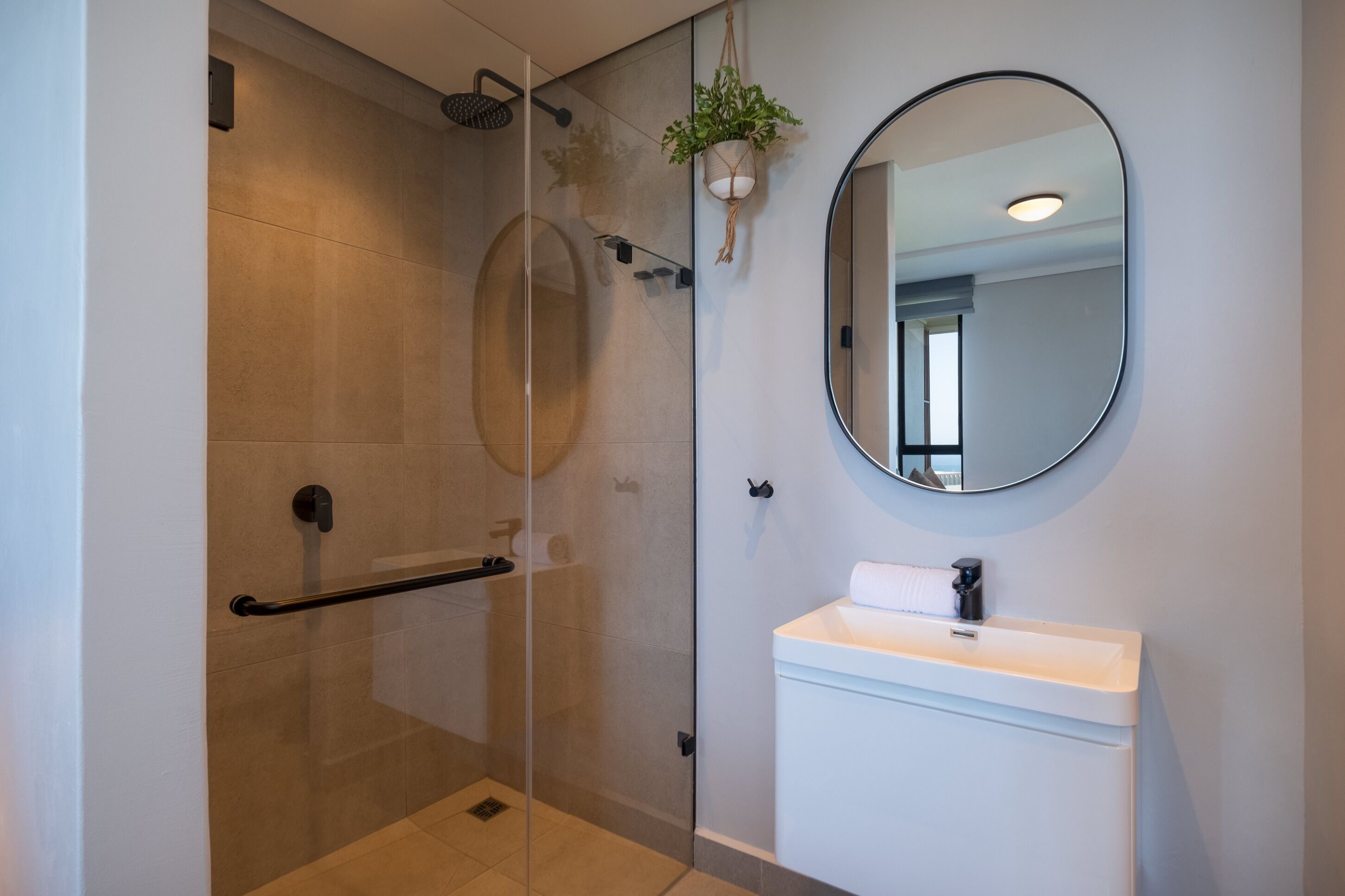 Une salle de bain moderne avec une douche à parois de verre, un lavabo blanc et un miroir rond.