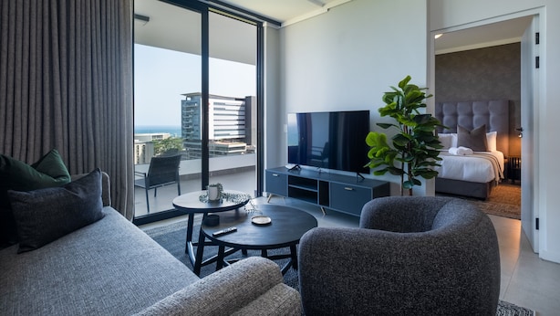 Ein modernes Hotelzimmer mit großem Balkon, einem Flachbildfernseher, einer Couch, einem Couchtisch und einem Bett mit Kopfteil.