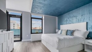 Ein modernes Schlafzimmer mit einem großen Bett, einem Nachttisch, einem Fenster mit Blick auf die Stadt und einem Balkon.