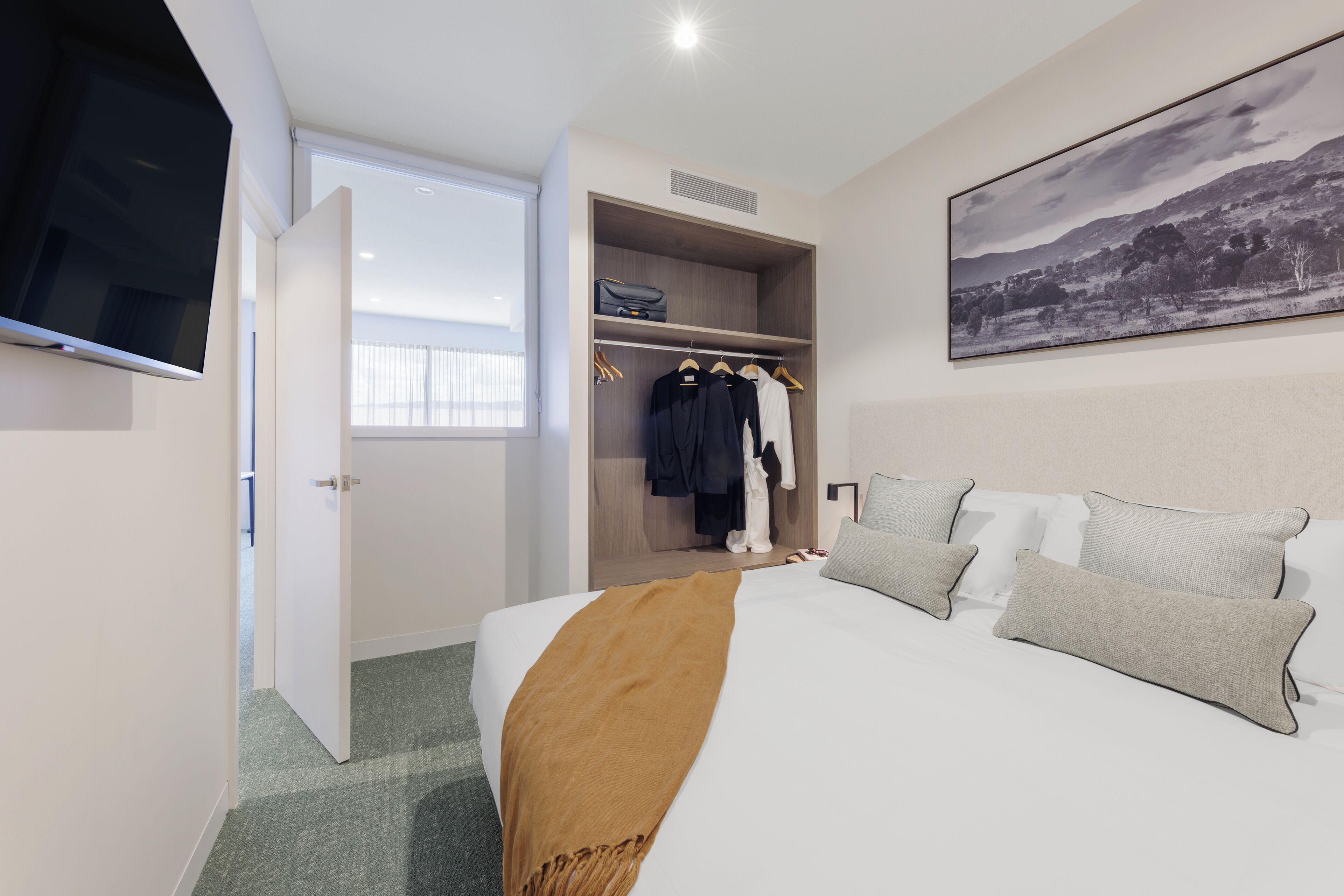 A hotel room with a bed, a wardrobe, a television, and a painting on the wall.