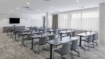 A conference room with tables and chairs, a flat-screen TV, and large windows with curtains.