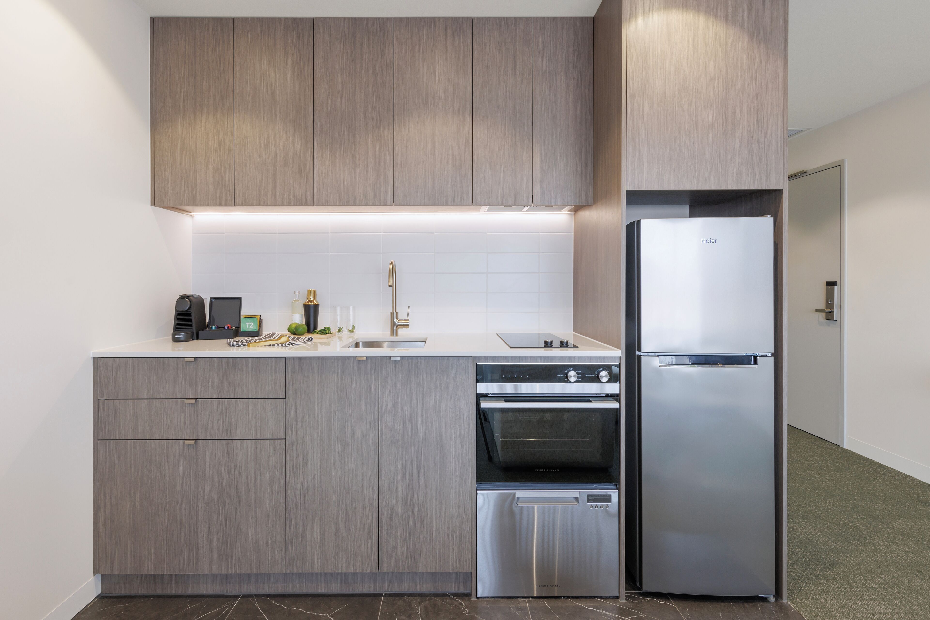 A modern kitchen with grey cabinetry, a built-in oven, a dishwasher, and a refrigerator.