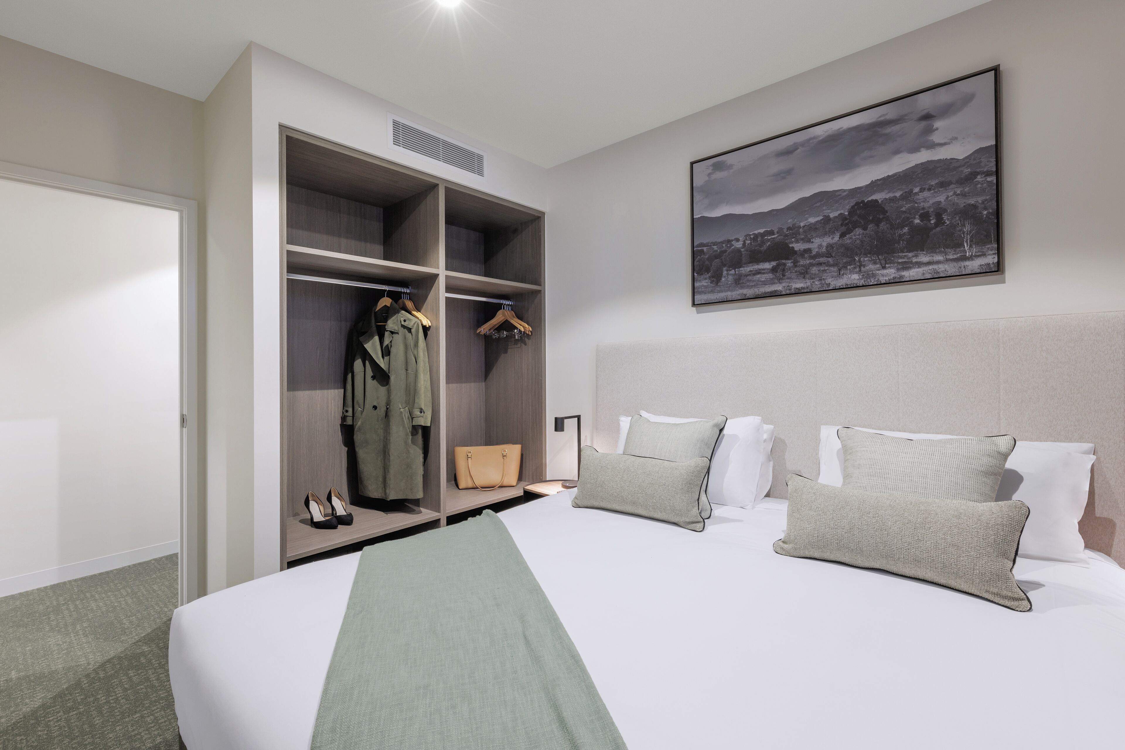 A hotel room with a large bed, a wardrobe with hanging clothes, a coat rack, and a framed picture on the wall.