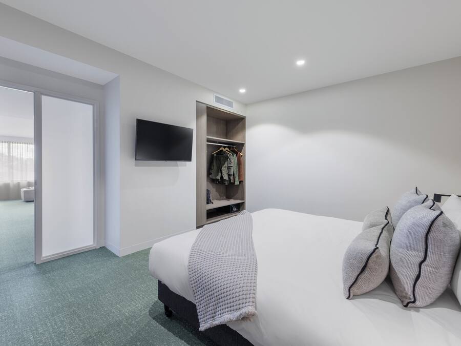 A hotel room with a bed, a wardrobe, a flat-screen TV, and a door leading to another room.