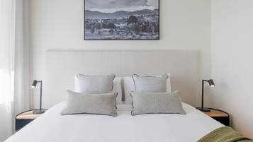 Ein ordentlich bezogenes Bett mit zwei Kissen und zwei Nachttischlampen, ein gerahmtes Landschaftsfoto über dem Bett und eine grüne Decke am Fußende.