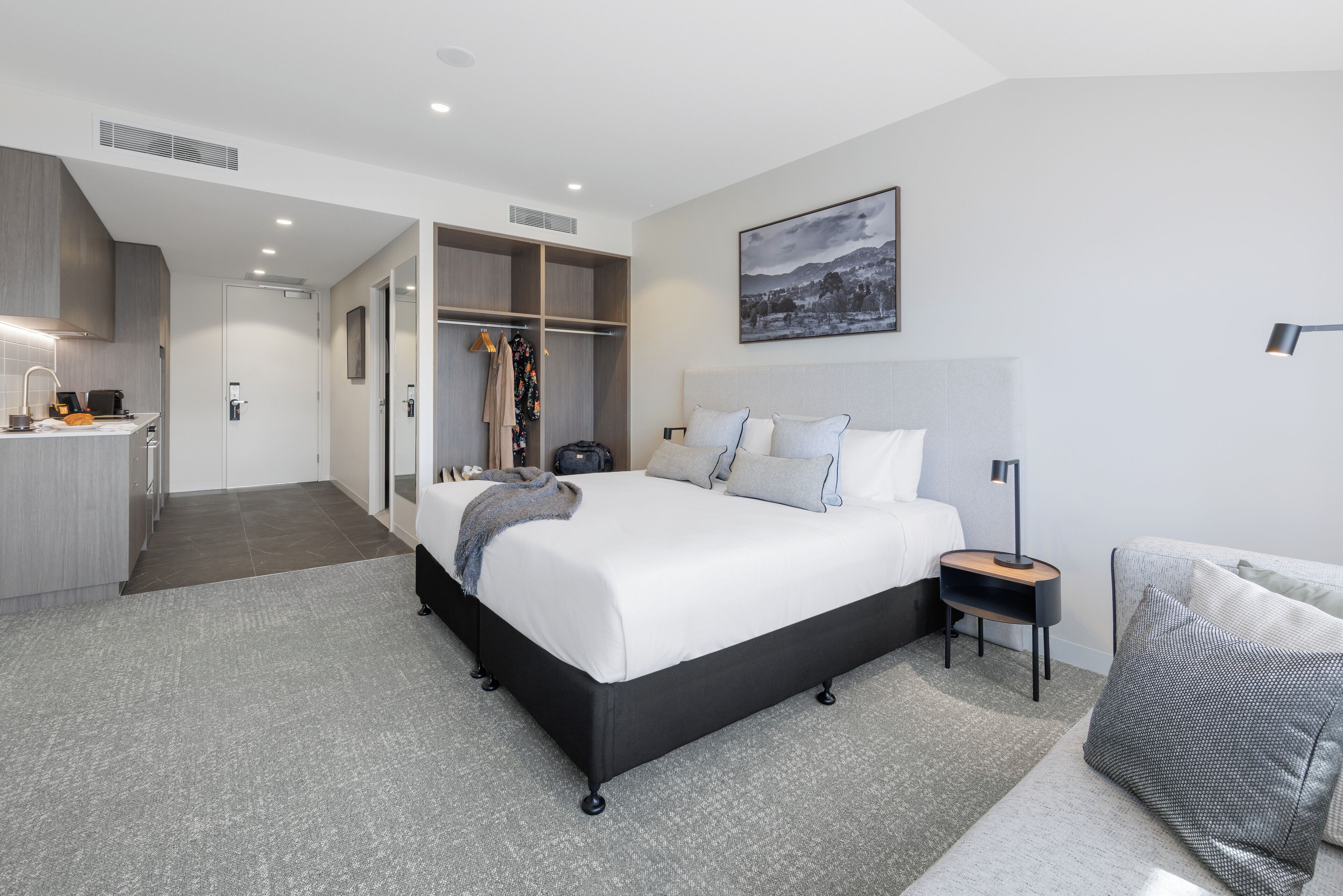 Ein modernes Hotelzimmer mit einem großen Bett, einem Nachttisch mit Lampe, einem Kleiderschrank und Blick auf die Stadt.