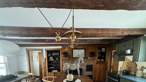 Une cuisine rustique avec un îlot central en bois, un luminaire en laiton suspendu et une cheminée en briques.