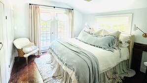 Une chambre avec un grand lit, un ventilateur de plafond, une chaise et une fenêtre avec des rideaux.