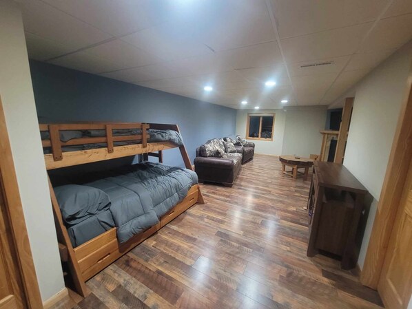 A room with a bunk bed, a sofa, a small table, and a window.