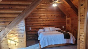 Un dormitorio rústico tipo cabaña con una cama, un ventilador de techo y una mesita de noche.