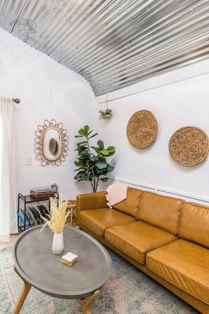 A living room with a brown leather sofa, a round coffee table, a mirror, and a potted plant.