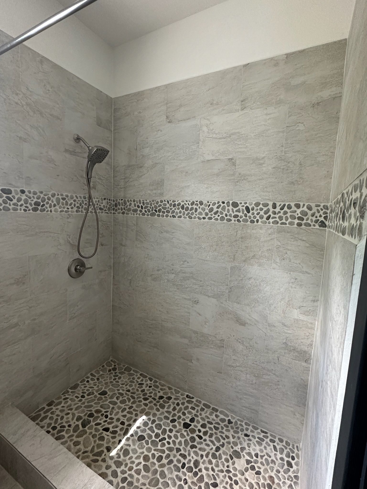 Eine Dusche mit Steinmosaik-Boden und Duschkopf aus Metall.