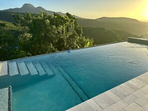 A swimming pool with clear water, surrounded by lush greenery and mountains in the background.