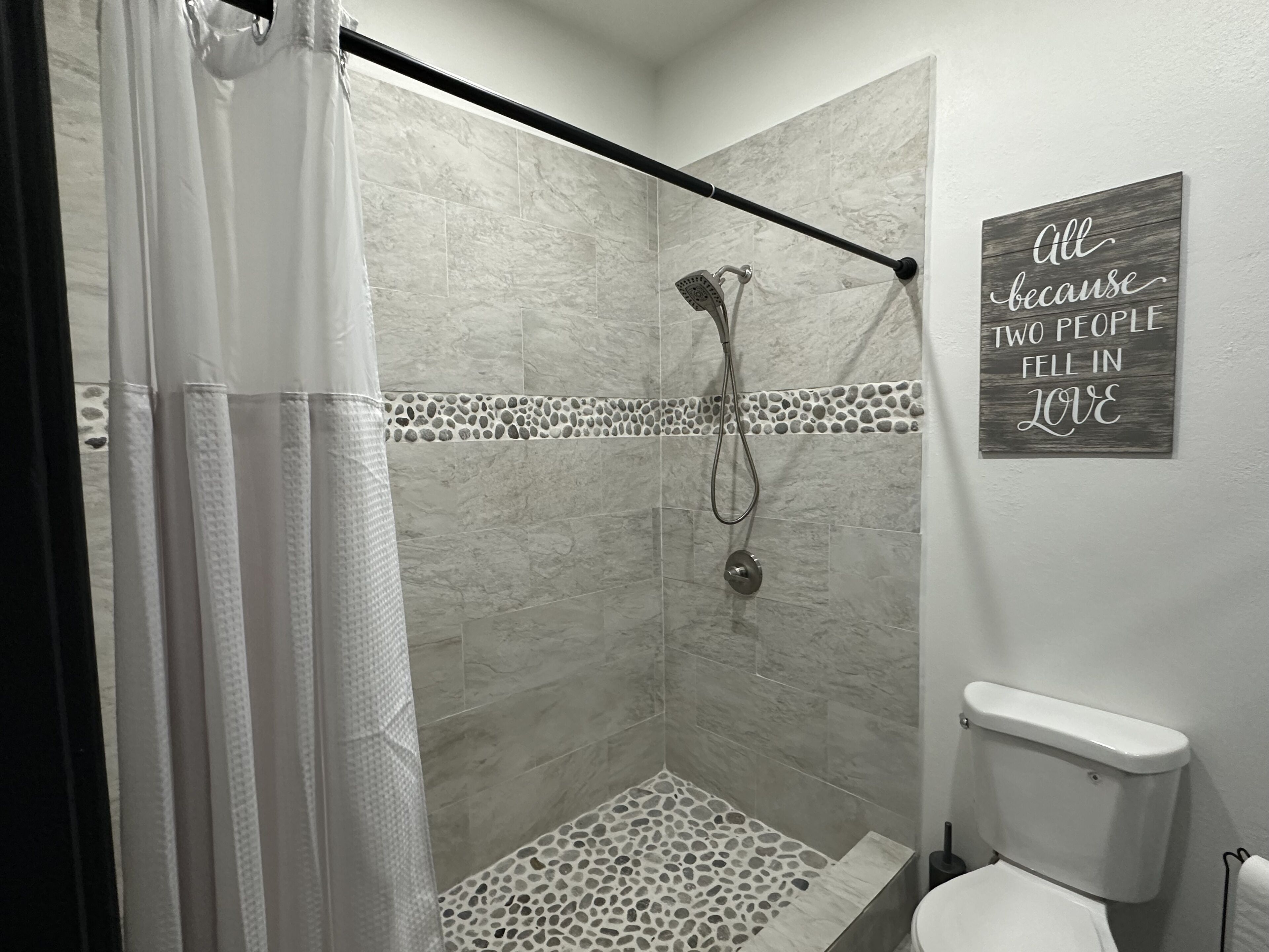 Un espace douche équipé d’un pommeau de douche, d’un porte-serviettes et d’une pancarte fixée au mur.