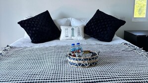 A neatly made bed with a nautical-themed pillow, a painting of sailboats, and a basket with snacks. - Belle La Maye - Triton (Castries)