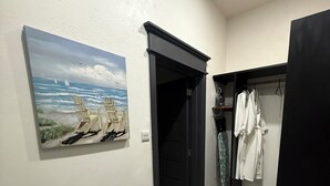 Een gang met een schilderij van een strand, een zwarte deur en een rek met witte gewaden.