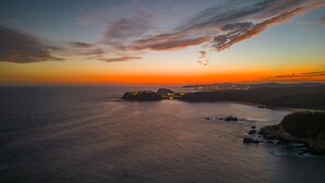 A coastal landscape at sunset with a rocky outcrop and a distant town.
