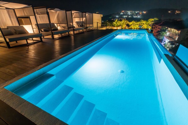 Una piscina con borde azul cristalino, rodeada de sillones de descanso y una cubierta de madera.