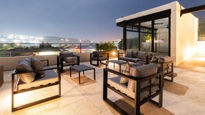 A rooftop terrace with outdoor seating, large windows, and a city view.