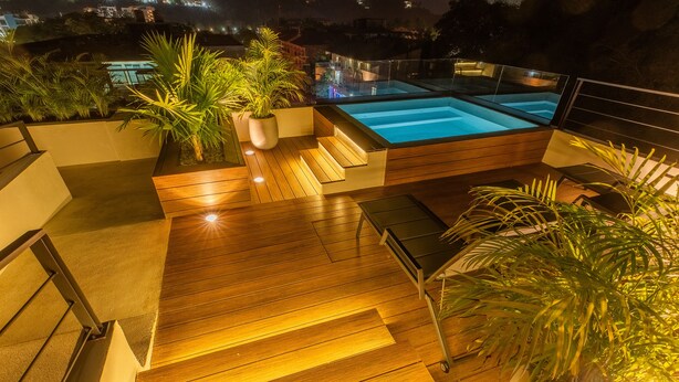 A rooftop pool area with wooden flooring, steps leading to the pool, and potted plants.