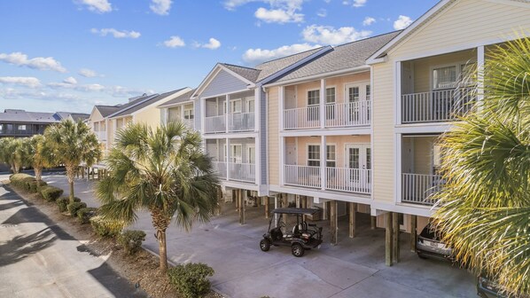 A beachfront hotel with multiple-story buildings, balconies, and palm trees. - Pool,1 Block to Beach, Sleeps 10, Golf Cart, Main ST (North Myrtle Beach)