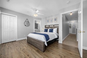A bedroom with a wooden bed, white walls, a ceiling fan, and a hallway leading to another room. - Pool,1 Block to Beach, Sleeps 10, Golf Cart, Main ST (North Myrtle Beach)
