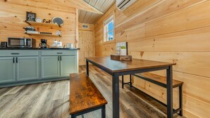 A wooden interior with a kitchen area featuring a microwave, coffee maker, and shelves with kitchenware.