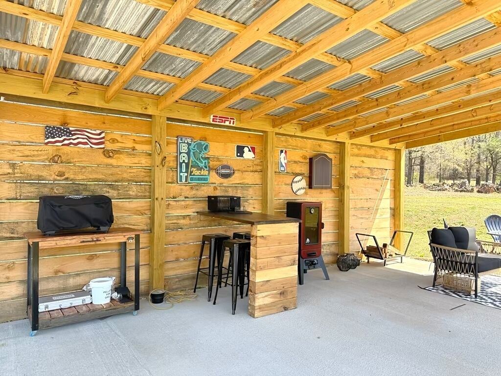 Een overdekt buitengebied met houten wanden, een bar, krukken en een grill.