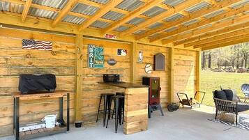 Een overdekt buitengebied met houten wanden, een bar, krukken en een grill.