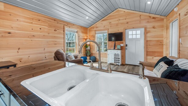 A wooden cabin interior with a large sink, wooden walls, a television, and a cozy seating area.