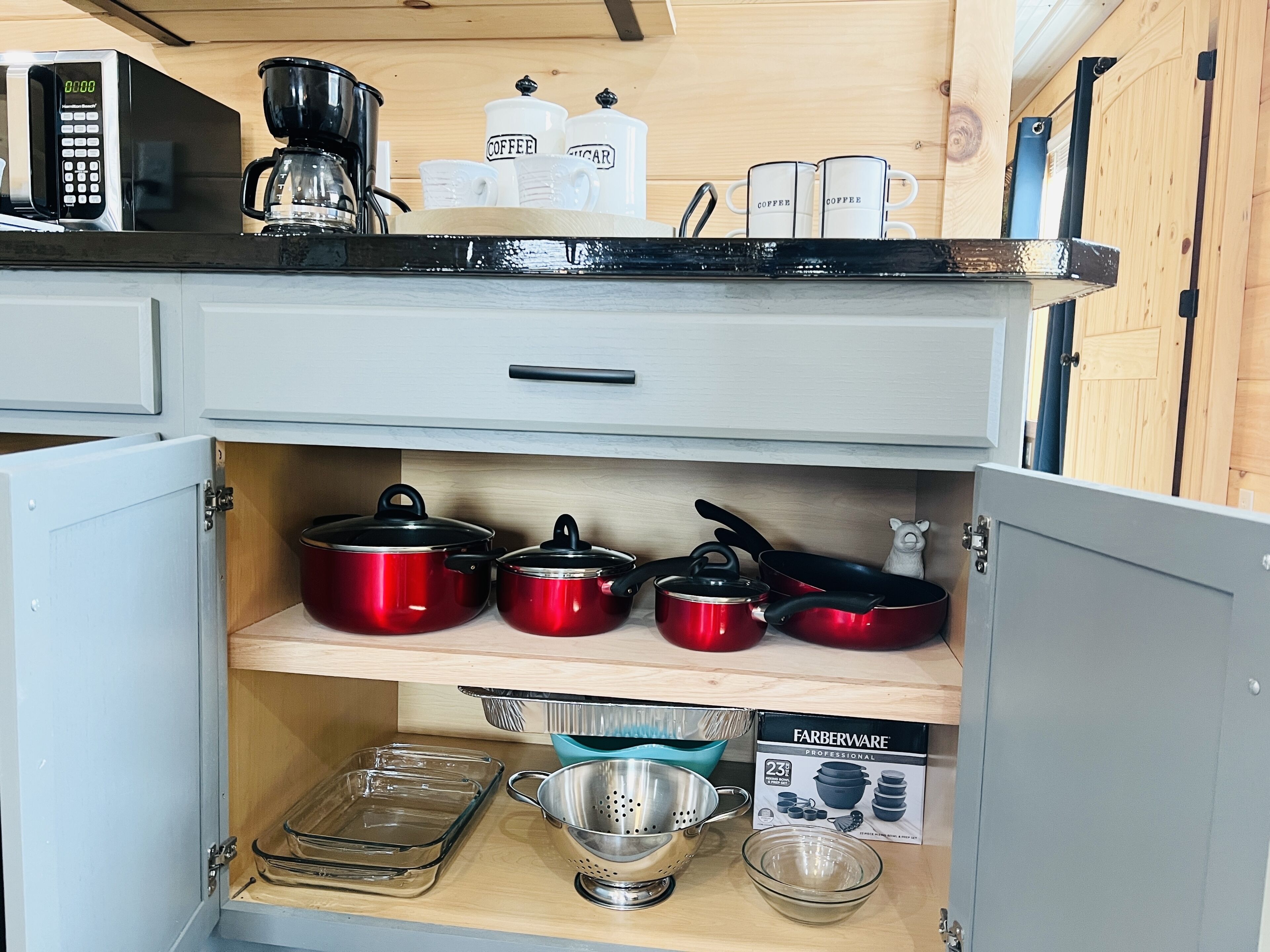 A kitchen with a microwave, coffee maker, and various pots and pans.