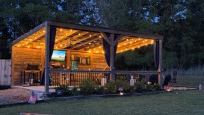 A wooden outdoor pavilion with string lights, a television, and a dartboard.