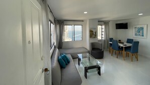 A modern living room with a sofa, a glass coffee table, and a dining area with chairs and a table. - Apartamento AL2-P Cerca al Mar con Pisci (Cartagena)