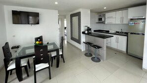 A modern kitchen with white cabinets, a black countertop, and stainless steel appliances. There is a dining area with a glass table and black chairs. - Apartamento AL2-P Cerca al Mar con Pisci (Cartagena)