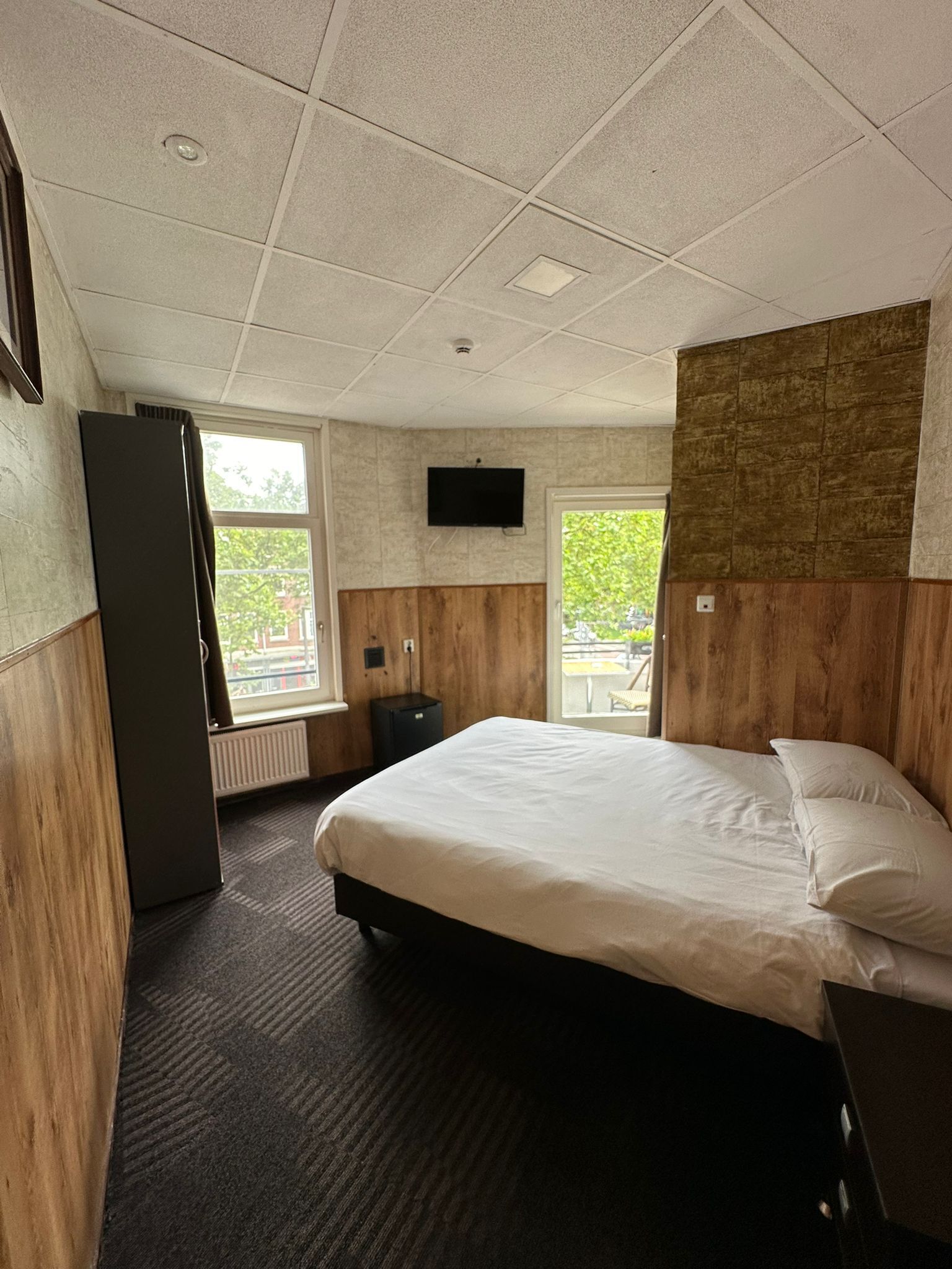 A hotel room with a bed, a television, a window, and a radiator.