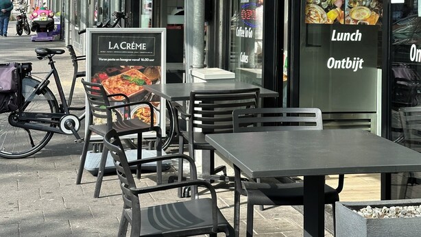 Un espacio al aire libre con mesas y sillas frente a un restaurante llamado "LA CREME".
