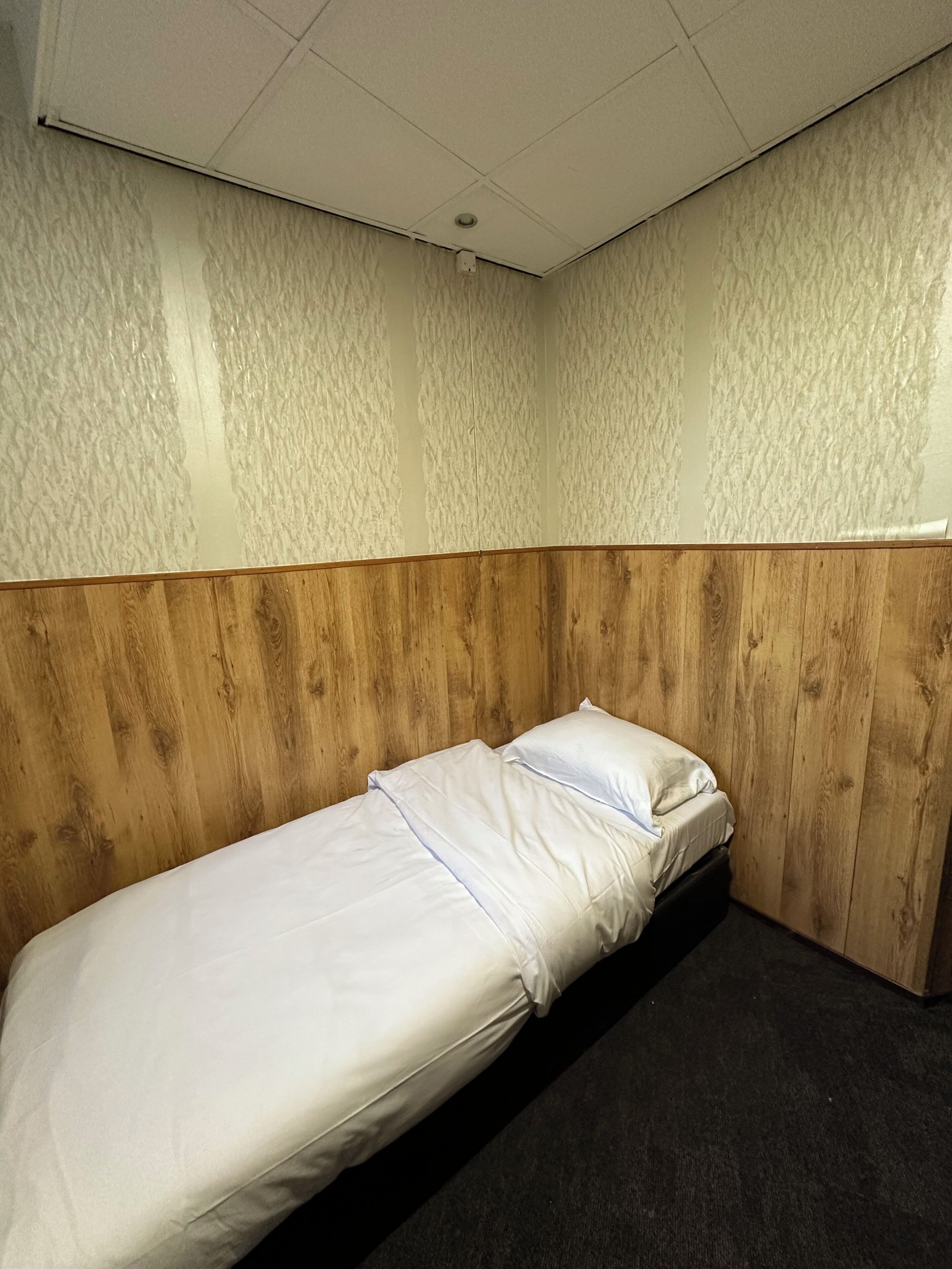 A single bed with white bedding in a room with textured walls and a wooden headboard.