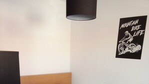 Una cama individual con una colcha a rayas y un cojín con forma de corazón, un cabecero negro, una lámpara de pared y un cartel en la pared.