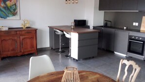 Una cocina moderna con armarios oscuros, una isla central y un comedor con una mesa redonda de madera y sillas.