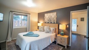 A bedroom with a bed, bedside lamps, a headboard, a nightstand, a door, and a window with curtains.