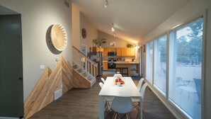 A modern kitchen with wooden cabinets, a dining area with a white table and chairs, and a staircase leading to another level.